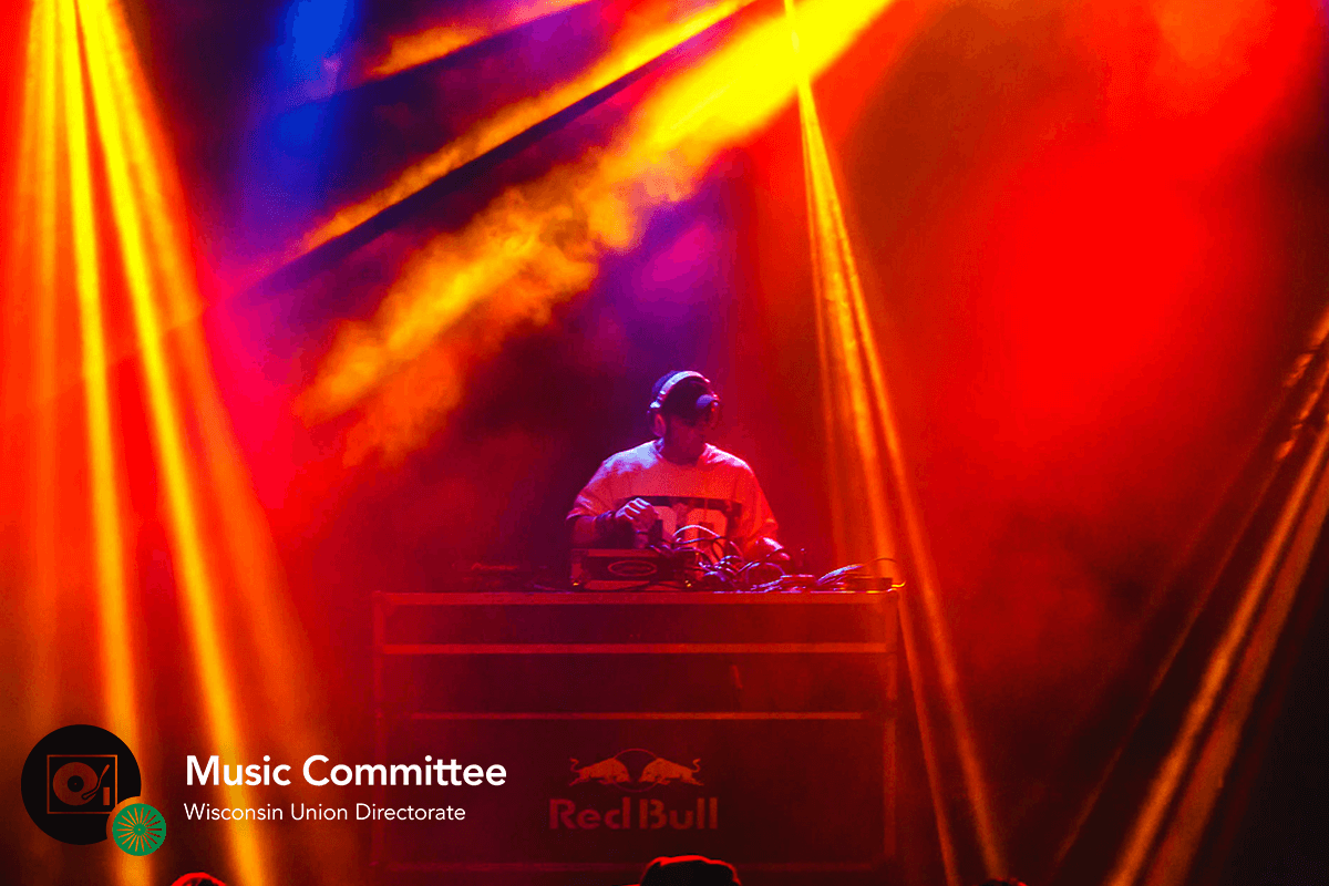 DJ performing on stage among red laser lights and fog
