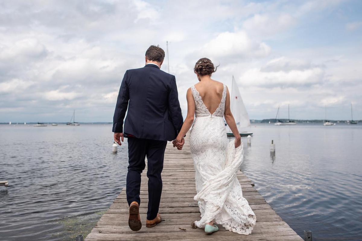 Bride and groom hold hands on a pier on Lake Mendota